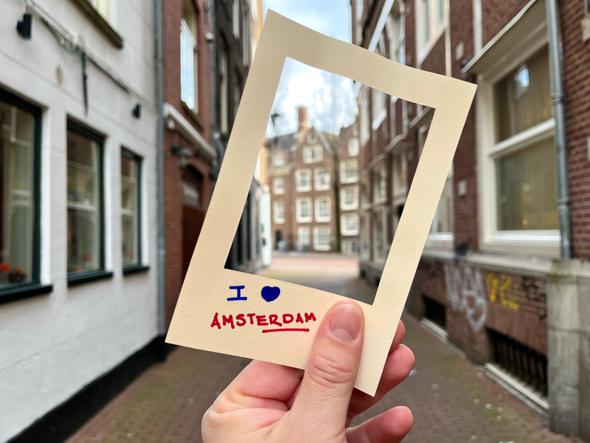 POV Point of view of latin backpacker tourist male holding a cardboard frame with i love Amsterdam written on it, framing a typical Dutch street in Amsterdam, Netherlands POV Point of view of latin backpacker tourist male holding a cardboard frame with i love Amsterdam written on it, framing a typical Dutch street in Amsterdam, Netherlands