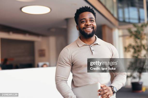smiling young businessman holding laptop walking in modern office - african american ethnicity stock pictures, royalty-free photos & images