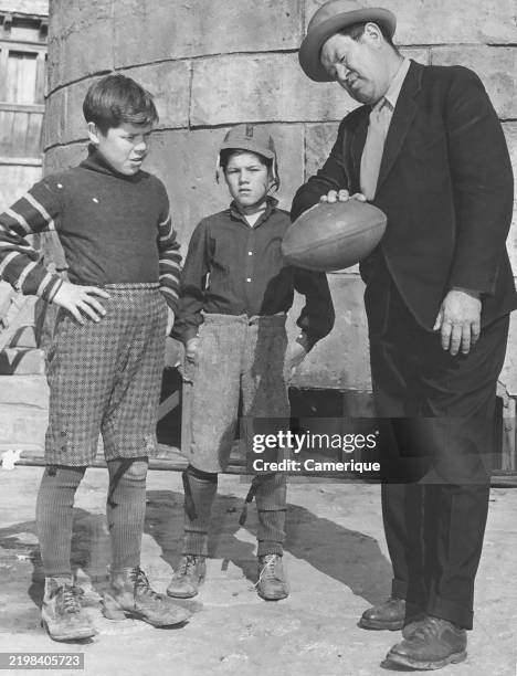 Football great Jim Thorpe is shown giving some passing tips to his son Phil and Bill on a movie lot where they are playing roles as sandlot, gridiron...