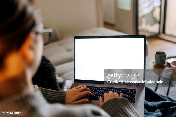 vue par-dessus l’épaule de la jeune femme utilisant un ordinateur portable avec un écran blanc vide tout en se relaxant sur un canapé à la maison - écran blanc photos et images de collection