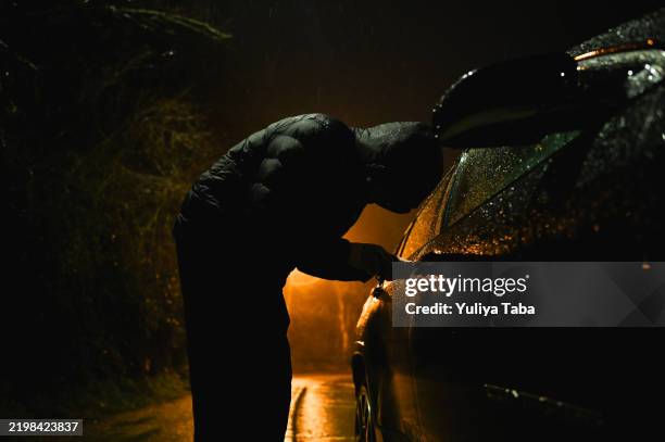 un homme avec une cagoule tente de s’introduire dans une voiture. - voleur photos et images de collection