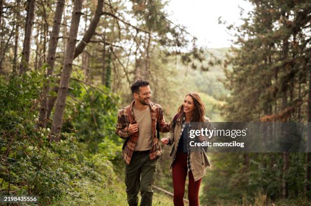 happy young couple hiking through nature - beschermd natuurgebied stockfoto's en -beelden