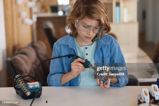 schuljunge arbeitet zu hause an seinem roboter - lötkolben stock-fotos und bilder