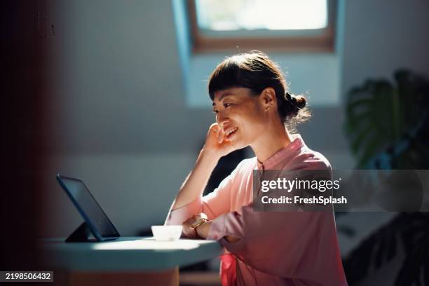 smiling woman in bright room using tablet for work or entertainment - using digital tablet stock pictures, royalty-free photos & images