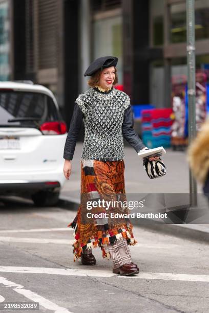 Chloe King wears black beret, black long sleeve shirt, silver beaded sheer mesh top, dark orange pattern/print scarf midi skirt, light brown pattern...