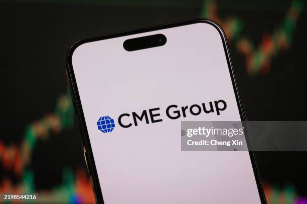 In this photo illustration, the CME Group logo is displayed on a smartphone screen in front of a stock chart showcasing CME Group's financial...