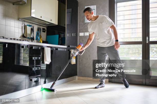 man vacuuming floor with a cordless vacuum cleaner - aufgeräumter raum stock-fotos und bilder