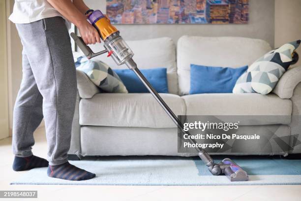 man cleaning a rug with a cordless vacuum cleaner - aspirapolvere foto e immagini stock