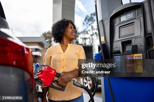 Happy woman refueling her car at a petrol station and smiling Happy woman refueling her car at a petrol station and smiling