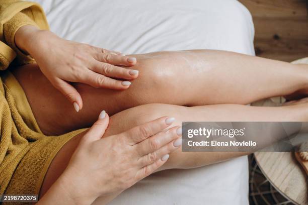 woman applies moisturizing lotion to her thigh skin, body cream after showering - crema corporal fotografías e imágenes de stock