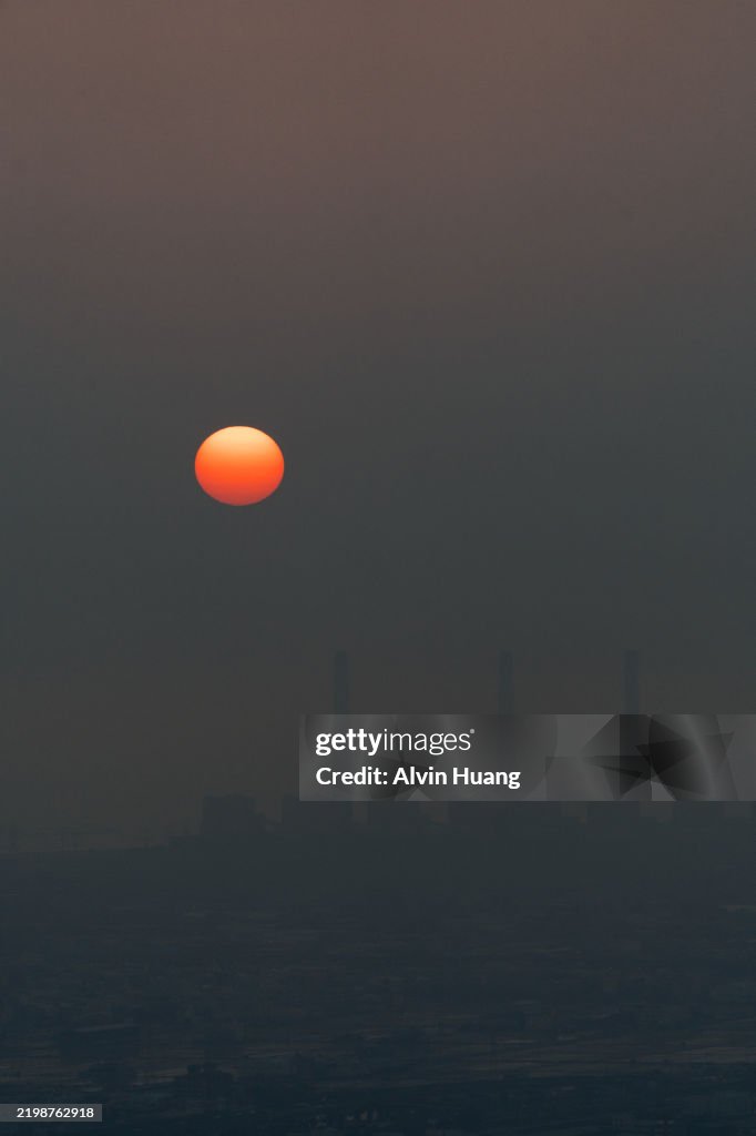 The sunset, like a golden egg yolk, slowly descends over the sea. Through the thick mist, the towering chimneys of the Taichung Power Plant faintly emerge in the background.