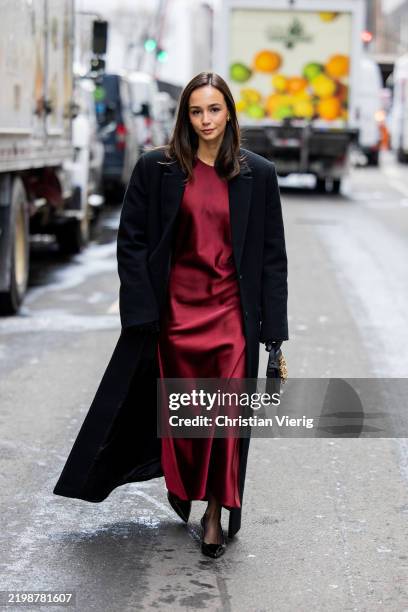 Blanca Arimany wears red silk dress, black coat, bag outside Carolina Herrera during New York Fashion Week on February 10, 2025 in New York City.
