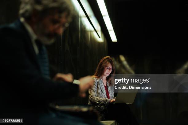 donna d'affari che lavora a tarda notte sul suo computer portatile in una sala d'attesa buia - person on computer in dark room foto e immagini stock