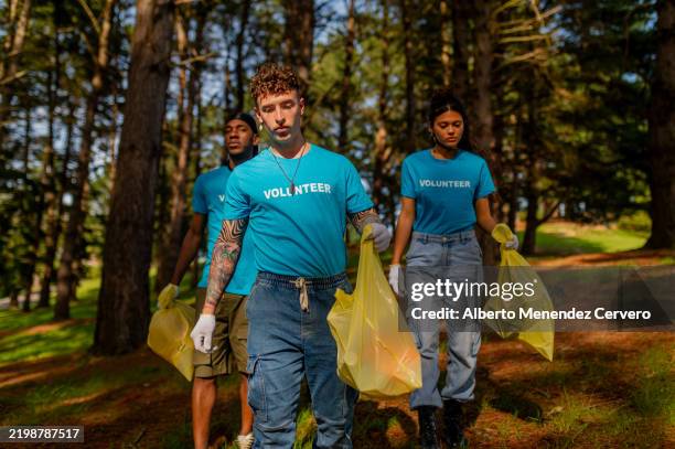 volunteers collecting trash in forest wearing blue shirts - public service stock pictures, royalty-free photos & images