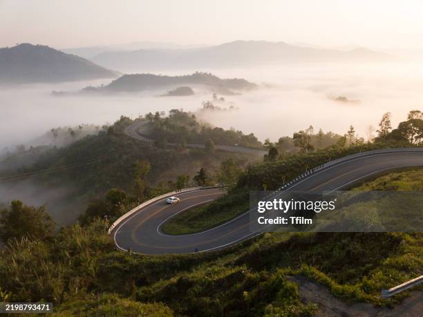 winding road emerging through dense morning fog - driving mountain road stock pictures, royalty-free photos & images