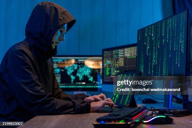 anonymous computer hacker in white mask and hoodie. obscured dark face using laptop computer for cyber attack and calling on cellphone, data thief, internet attack, darknet and cyber security concept. - scammer trickbetrüger stock-fotos und bilder