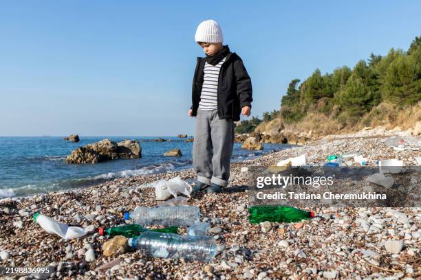 a child stands on the beach surrounded by plastic waste. - littering stock pictures, royalty-free photos & images
