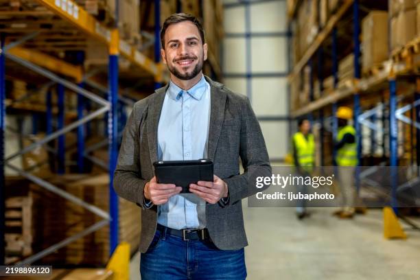 young businessman using tablet in warehouse with workers in background - inventory management stock pictures, royalty-free photos & images