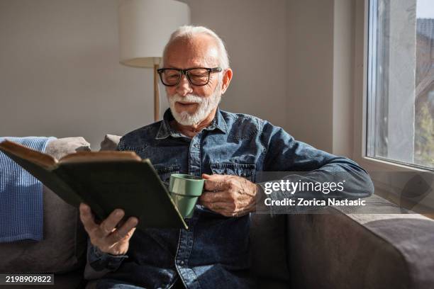senior man is reading book with a cup of coffee - reading glasses stock pictures, royalty-free photos & images