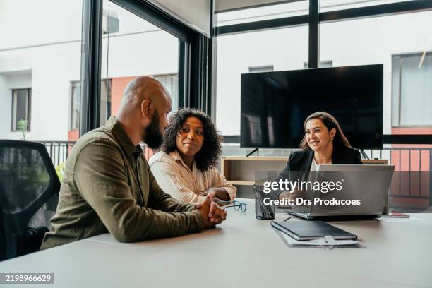 couple talking to real estate agent in office - estate agency stock pictures, royalty-free photos & images