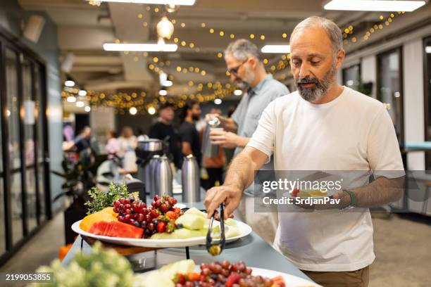people serving food at social event buffet in brightly lit modern setting - buffet stockfoto's en -beelden