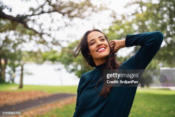 frau lächelt im freien in einem park unter natürlichem licht - hand in den haaren stock-fotos und bilder