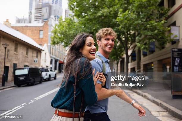happy young couple smiling together on a city street walk - couple crossing street stock pictures, royalty-free photos & images