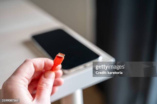 hand showing orange type c charging cable with smartphone in background, waiting for charge - cargador de móvil fotografías e imágenes de stock