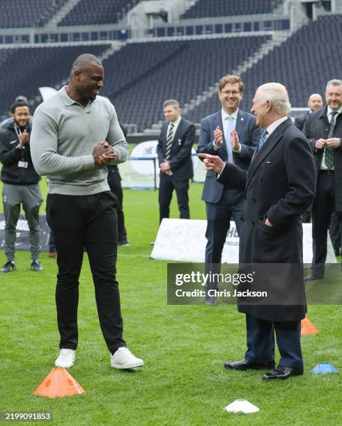 King Charles III and Efe Obada share a joke as they attend a demonstration by young people involved in The Huddle Project at Tottenham Hotspur...