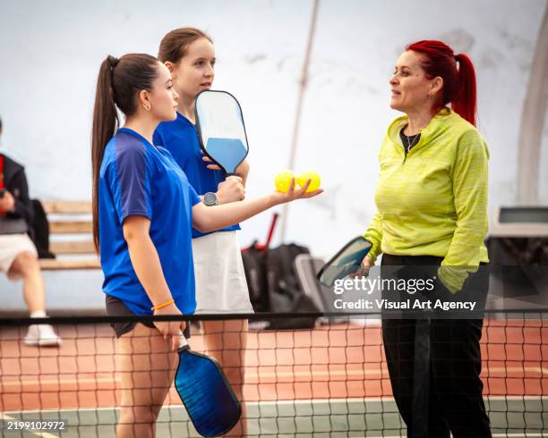 two teenager and one senior pickleball coach are talking next to sport net horizontal pickleball still - tennis ball art stock pictures, royalty-free photos & images