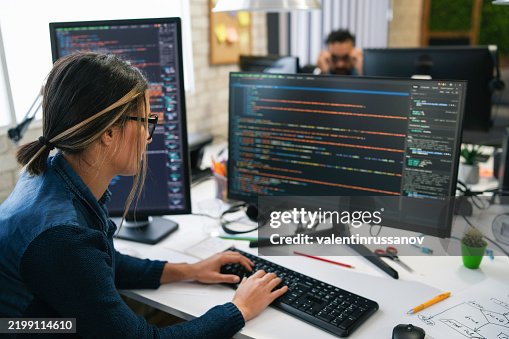 Female freelance developer coding and programming. Coding on two with screens with code language and application Female freelance developer coding and programming. Coding on two with screens with code language and application
