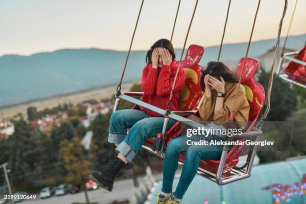 female friends feeling dizzy on high chain swing ride covering eyes trying not to throw up - fobia imagens e fotografias de stock