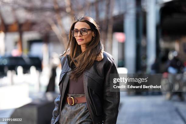 Guest wears dark brown sunglasses, dark brown sweater, dark brown oversized aviator leather jacket light brown shearling collar, dark brown leather...