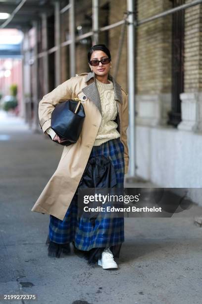 Guest wears black sunglasses, gold earrings, cream cable knit sweater, light brown tan Coach wind coat, shiny black large Coach leather bag, dark...