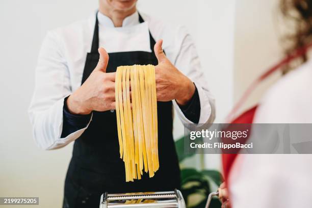 chef proudly showing fresh pasta from pasta machine - fettuccine stock pictures, royalty-free photos & images