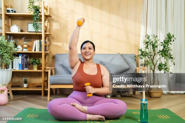 smiling woman performing at-home fitness routine with dumbbells on yoga mat - comfort zone stock pictures, royalty-free photos & images