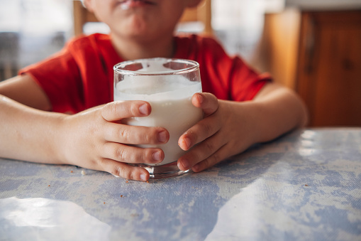 Children's hands holding a glass of milk at the table