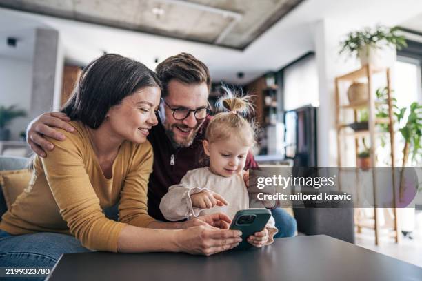 glückliche familie mit smartphone zu hause: eltern und tochter surfen im internet - websurfen stock-fotos und bilder