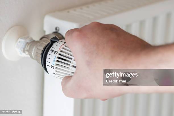 human hand adjusts thermostat on a heater - température photos et images de collection