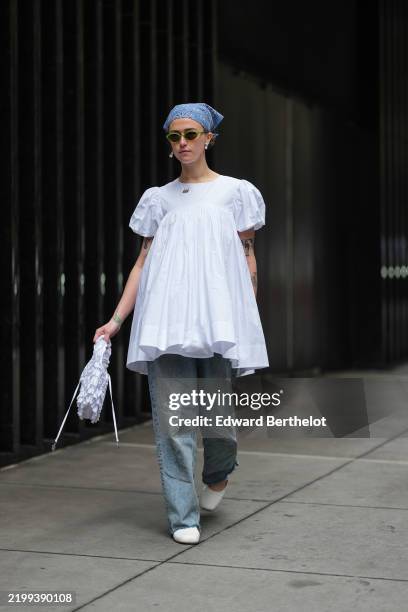 Ella Emhoff wears a bandanna, sunglasses, a white gathered mini dress with puff shoulders, blue denim pants / jeans , white shoes, outside Sandy...