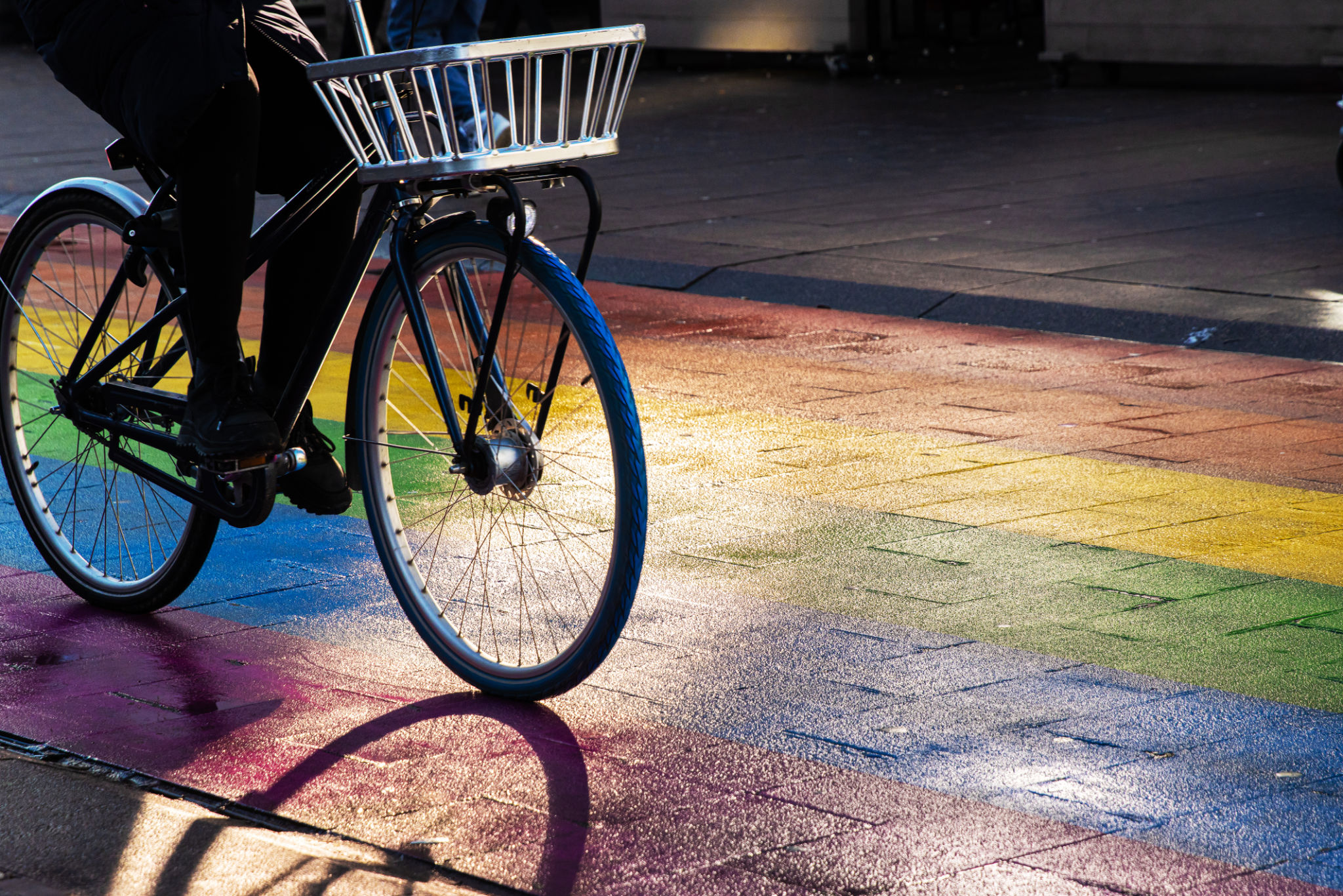 Cyclist riding a bicycle with a metal front basket on a rainbow street. Regenboogvlag in the Grote Marktstraat in the center of the Hague, Netherlands. Selective focus. Movement effect Cyclist riding a bicycle with a metal front basket on a rainbow street. Regenboogvlag in the Grote Marktstraat in the center of the Hague, Netherlands. Selective focus. Movement effect