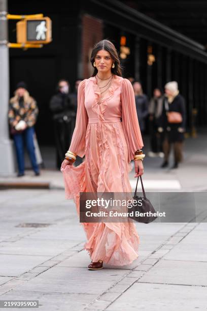 Guest wears gold earrings, black beaded layered necklaces, light pink long sleeve ruffled midi dress, cream dark brown layered bangle bracelets,...