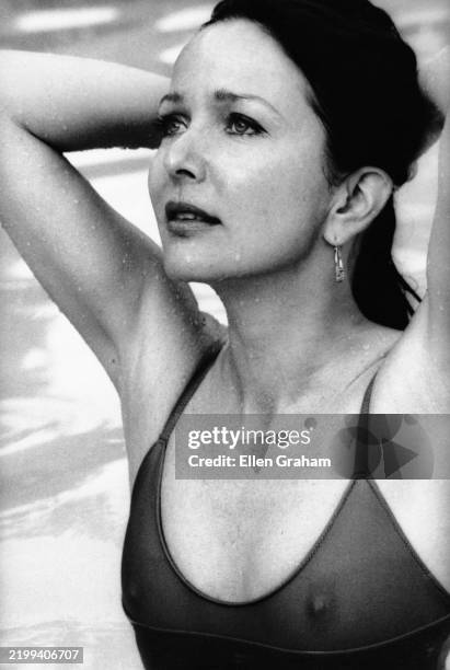 View of American actor Brooke Hayward, dressed in a semi-transparent swimsuit with her hands behind her head, as she stands in a pool at la Costa...