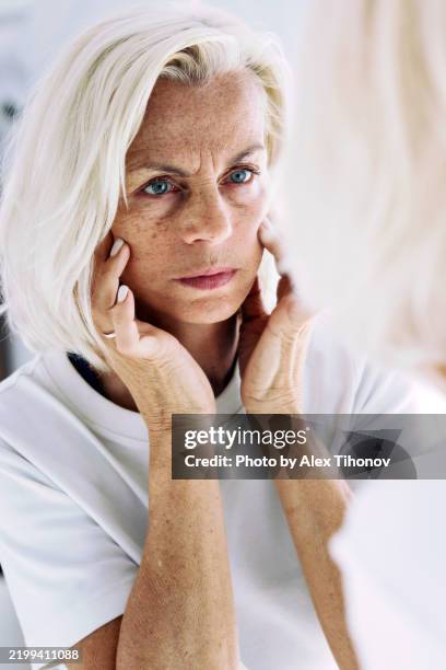 older woman touch her skin with dissatisfied expression due to wrinkles, ageing process and age changes - old woman face angry stock pictures, royalty-free photos & images
