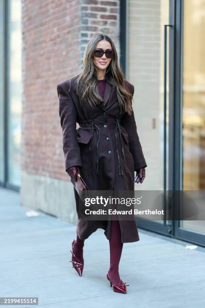 Tamara Kalinic wears dark brown sunglasses, burgundy bordeaux sweater, burgundy bordeaux wool coat, shiny burgundy bordeaux leather gloves, shiny...