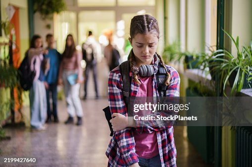 Sad teenage girl walks in school hallway while bullies tease her Sad teenage girl walks in school hallway while bullies tease her