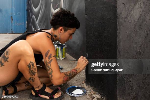 junge künstlerin, die ihr kunstwerk auf einem wandgemälde signiert - straßenmaler stock-fotos und bilder