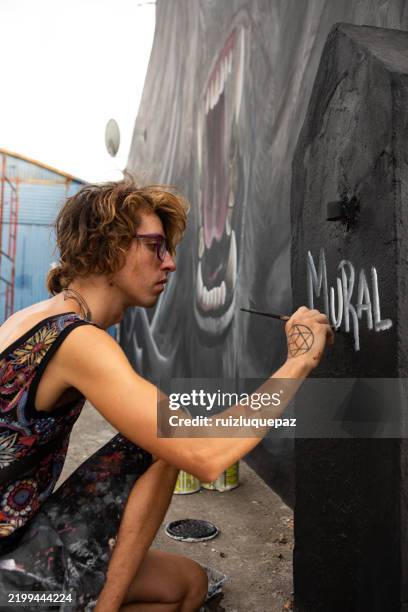 junge nicht-binäre künstler*innen, die ihre kunstwerke auf einem wandbild signieren - straßenmaler stock-fotos und bilder