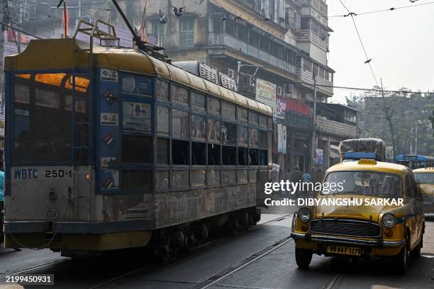 This photograph taken on January 28, 2025 shows passengers riding a Hindustan Ambassador yellow taxi past a tram, along a street in Kolkata. Kolkata...