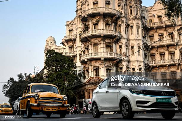This photograph taken on January 27, 2025 shows Hindustan Ambassador yellow taxis and a Tata Motors electric vehicle riding past the Esplanade...